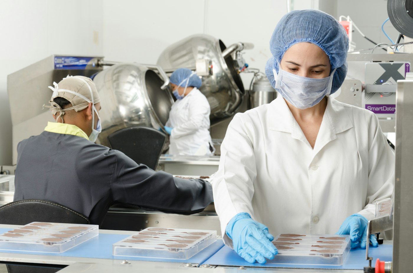 Opérateurs en tenue d'hygiène — charlotte, masque et gants — sur une ligne de conditionnement alimentaire